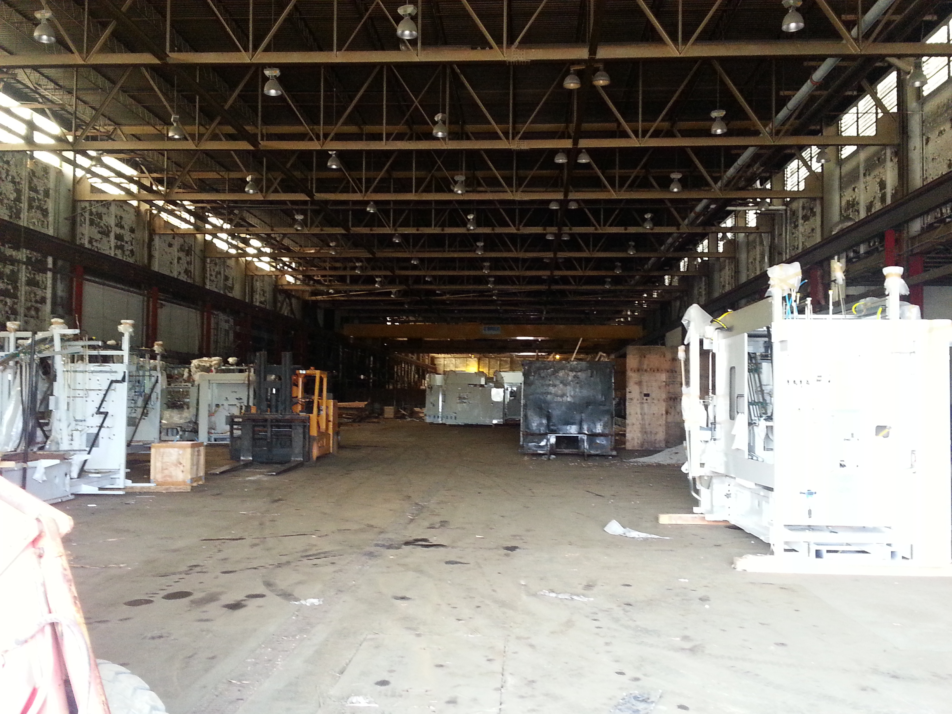 Inside the vacant former copper-tubing plant: an empty deteriorating industrial hall with steel trusses and abandoned machinery
