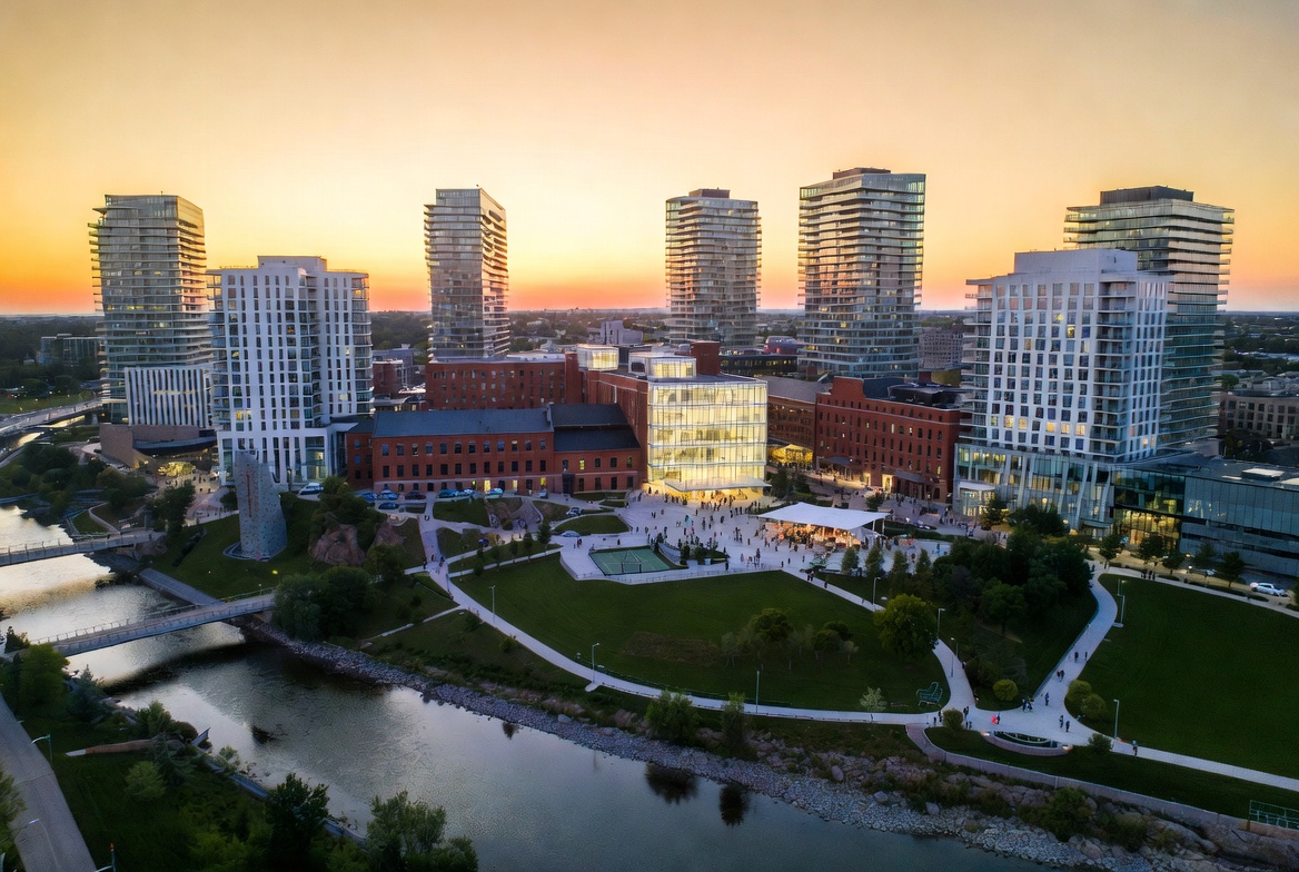 Aerial render of SPUR Smart Village at dusk - towers, mill, glass anchor building, civic plaza along the Speed River