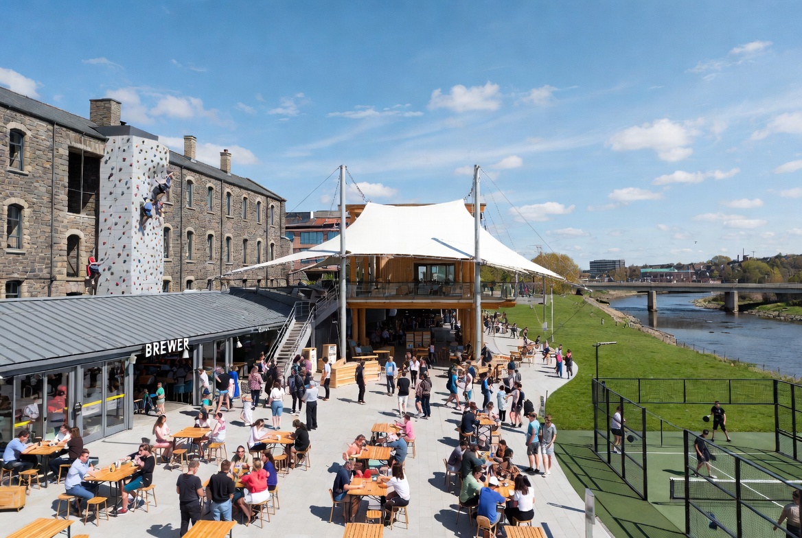 Riverside plaza with brewery, climbing wall, padel courts, and tent pavilion